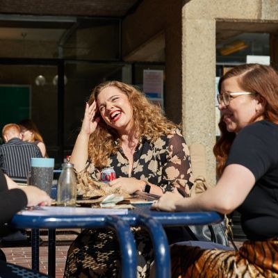 Students chatting at a bench table on lakeside terrace on a sunny day